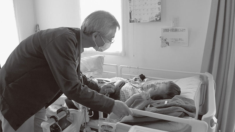 ベッドに横たわる伊鈴さんの手を握りながら声をかける瀬角医師の写真