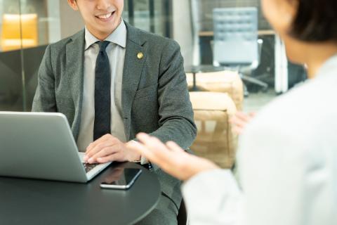 パソコンを開いて微笑む男性とその向かいで話す後ろ姿の女性の写真