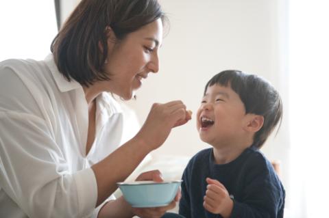 子どもにおやつを食べさせる若い母親の写真