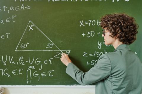 黒板に方程式を書くカーリーヘアの白人男性の写真。